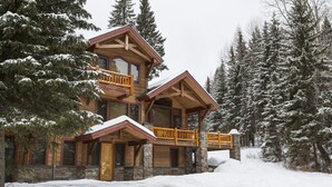 Una cabaña de troncos de varios pisos con cimientos de piedra, balcones de madera y un paisaje cubierto de nieve.