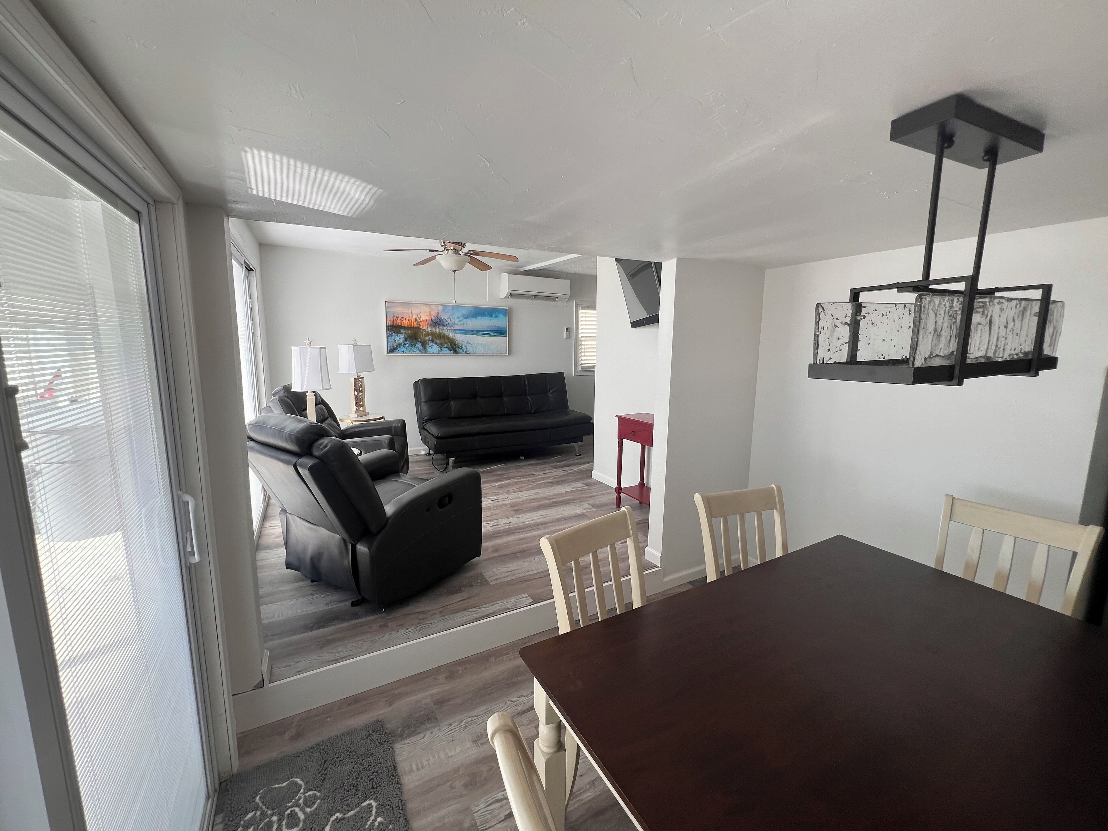 Una sala moderna con un sofá negro, una mesa de comedor con sillas y un ventilador de techo.