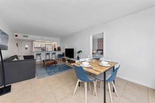 Una sala moderna con un sofá, una mesa de comedor para cuatro personas y una cocina al fondo.