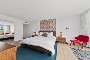 A modern hotel room with a large bed, bedside tables, a red chair, and a view of the outdoors.
