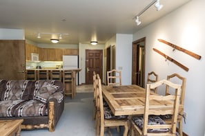 Un salon chaleureux avec une table et des chaises en bois, un canapé à motifs et une cuisine en arrière-plan.