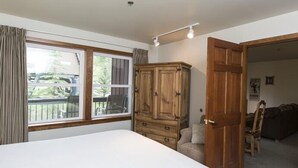 A bedroom with a large bed, wooden wardrobe, and a window with curtains. - Spacious Condo with Slope Access (Whitefish)