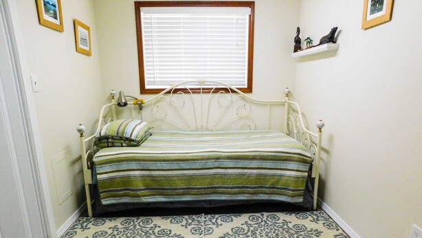 A small, neatly arranged bedroom with a single bed, a patterned rug, and a window with blinds.