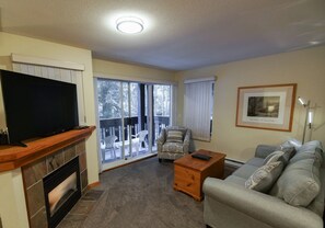 A living room with a television, sofa, coffee table, and a fireplace. - Stoney Creek Lagoons 32 (Whistler)