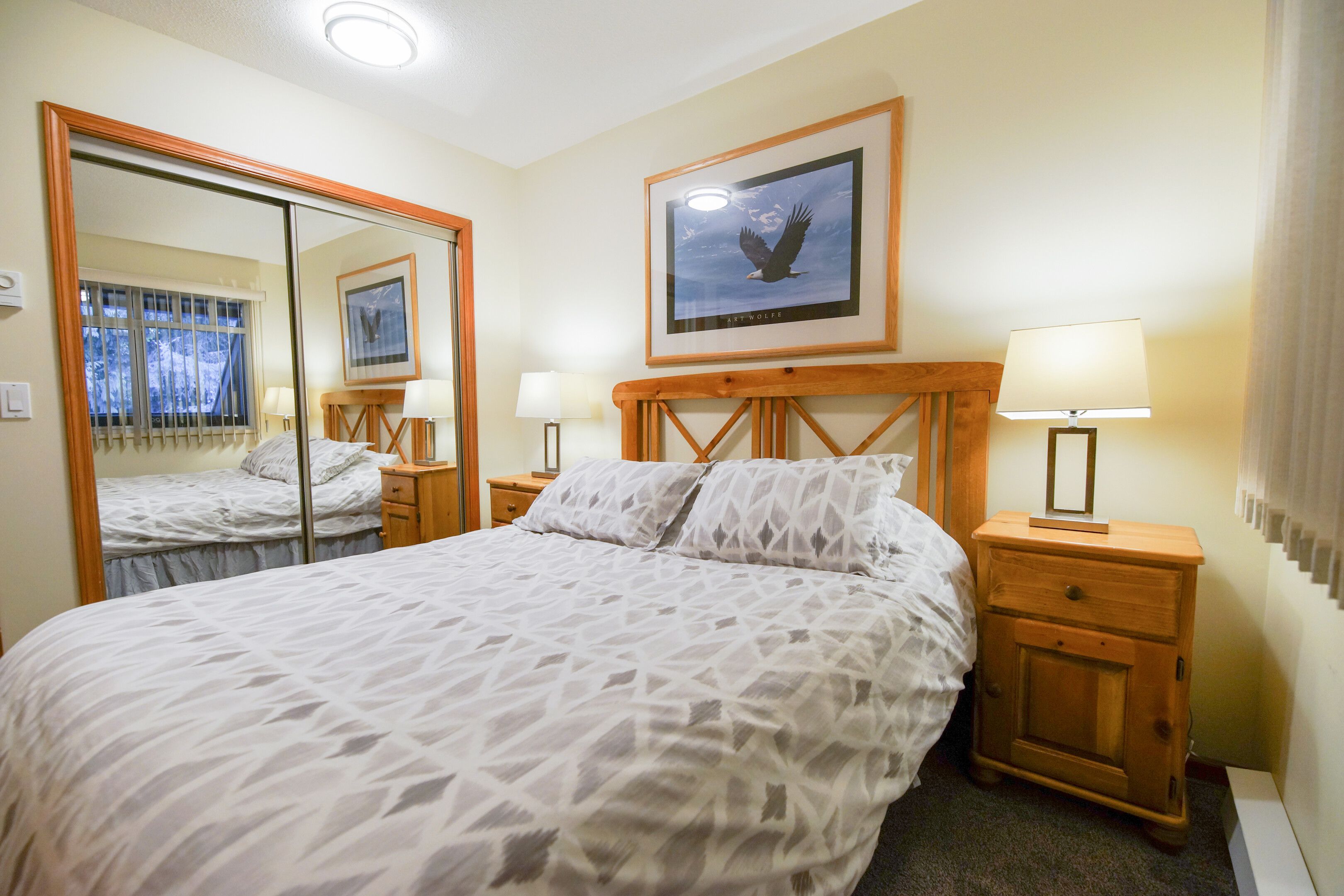 A hotel room with a large bed, two bedside tables with lamps, a mirror, and a framed picture on the wall.
