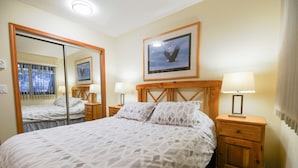 Quarto de hotel com uma cama grande, uma mesa de cabeceira de madeira, um espelho e um quadro com a imagem de uma águia.