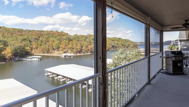 A balcony with a view of a lake, docked boats, and a forested hillside.