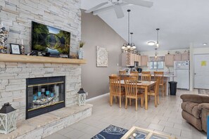 Ein modernes Wohnzimmer mit Kamin aus Stein, Essbereich, Küche und Deckenventilator.