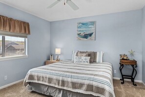 A bedroom with a bed, a nightstand, a lamp, a painting, and a window with blinds.