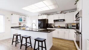Una cocina moderna con armarios blancos, un refrigerador negro, un lavamanos de acero inoxidable y una isla grande con taburetes de bar.