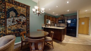 A dining area with a round table and chairs, a kitchen with wooden cabinets and appliances, and a large tapestry on the wall.
