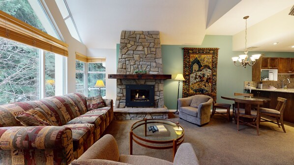 A cozy living room with a stone fireplace, a sofa, a round coffee table, and a view of the outdoors.