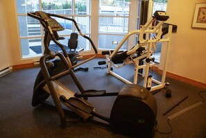A gym with exercise equipment, large windows, and a view of the outside.