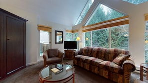 A living room with a sofa, armchair, television, and a glass coffee table.