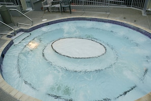 A circular hot tub with a tiled edge, surrounded by a concrete deck and metal railings.