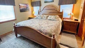 Ein Schlafzimmer mit einem hölzernen Bett, zwei Nachttischen, einem Schreibtisch, einem Deckenventilator, einem Fenster mit Jalousien und einem Teppich.