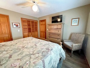A bedroom with a bed, a dresser, a chair, a TV, and wooden closets.