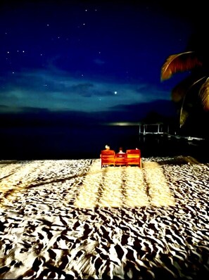 Sit on a beach bench under the starry night sky, surrounded by palm trees and a tranquil atmosphere.
