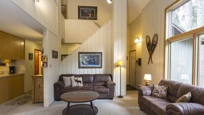 A spacious living area with a brown leather sofa, a coffee table, and a staircase leading to an upper level. - Spacious Home with Ski Access (Whitefish)