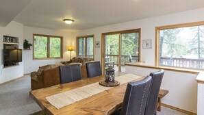 A dining area with a wooden table, black chairs, and a large window with a view of trees. - Spacious Home with Ski Access (Whitefish)