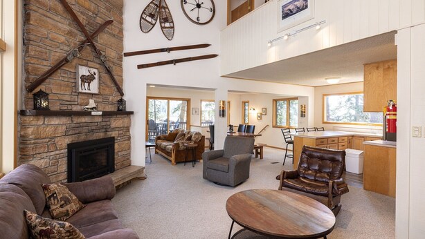 A spacious living room with a stone fireplace, a dining area, and a kitchen. - Spacious Home with Ski Access (Whitefish)