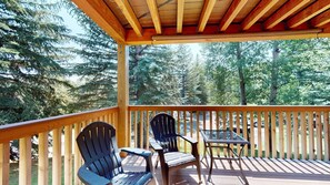 A wooden deck with two Adirondack chairs and a small table, overlooking a forested area.