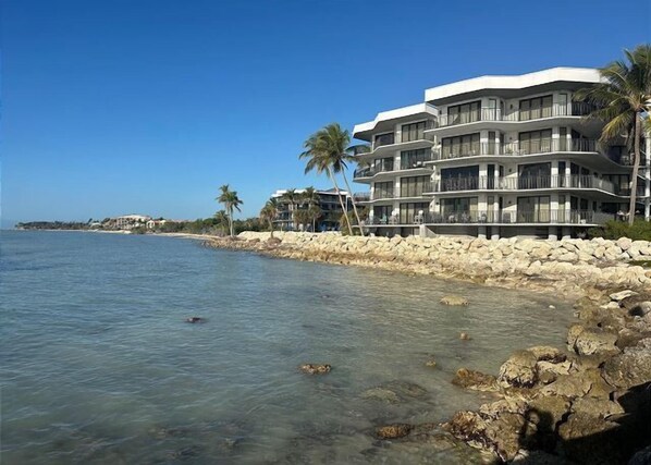 A beachfront hotel with multiple balconies, clear blue water, and palm trees.