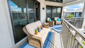 A balcony with wicker furniture, including a sofa and chairs, and a blue striped rug.