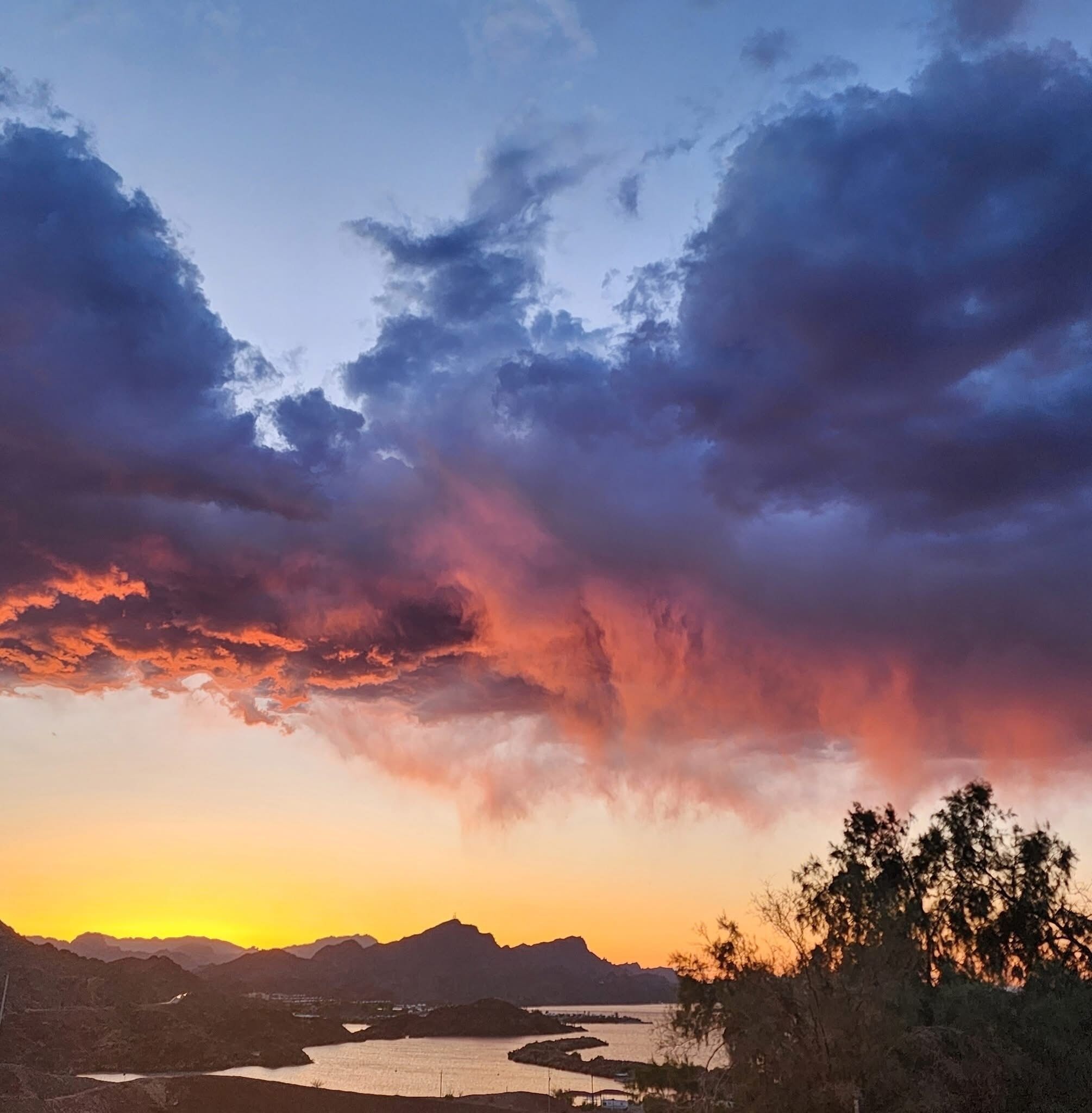 Un coucher de soleil sur un paysage montagneux, avec une rivière et un lac.
