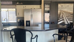 A kitchen with a bar area, two bar stools, a refrigerator, and a coffee maker. - Lake view home with mountain views by Havasu Springs (Parker)