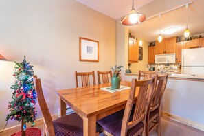 A dining area with a wooden table, chairs, a Christmas tree, and a kitchen in the background.