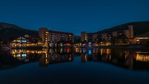 Ett hotell vid en sjö med flera byggnader som speglas i vattnet, omgivet av berg.