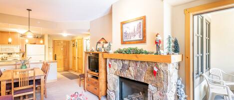 A cozy living room with a fireplace, a dining area, and a kitchen.
