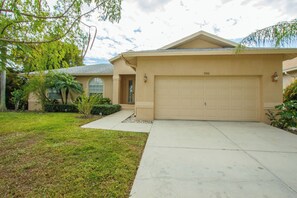 A single-story house with a beige garage door, a well-maintained lawn, and a clear sky.