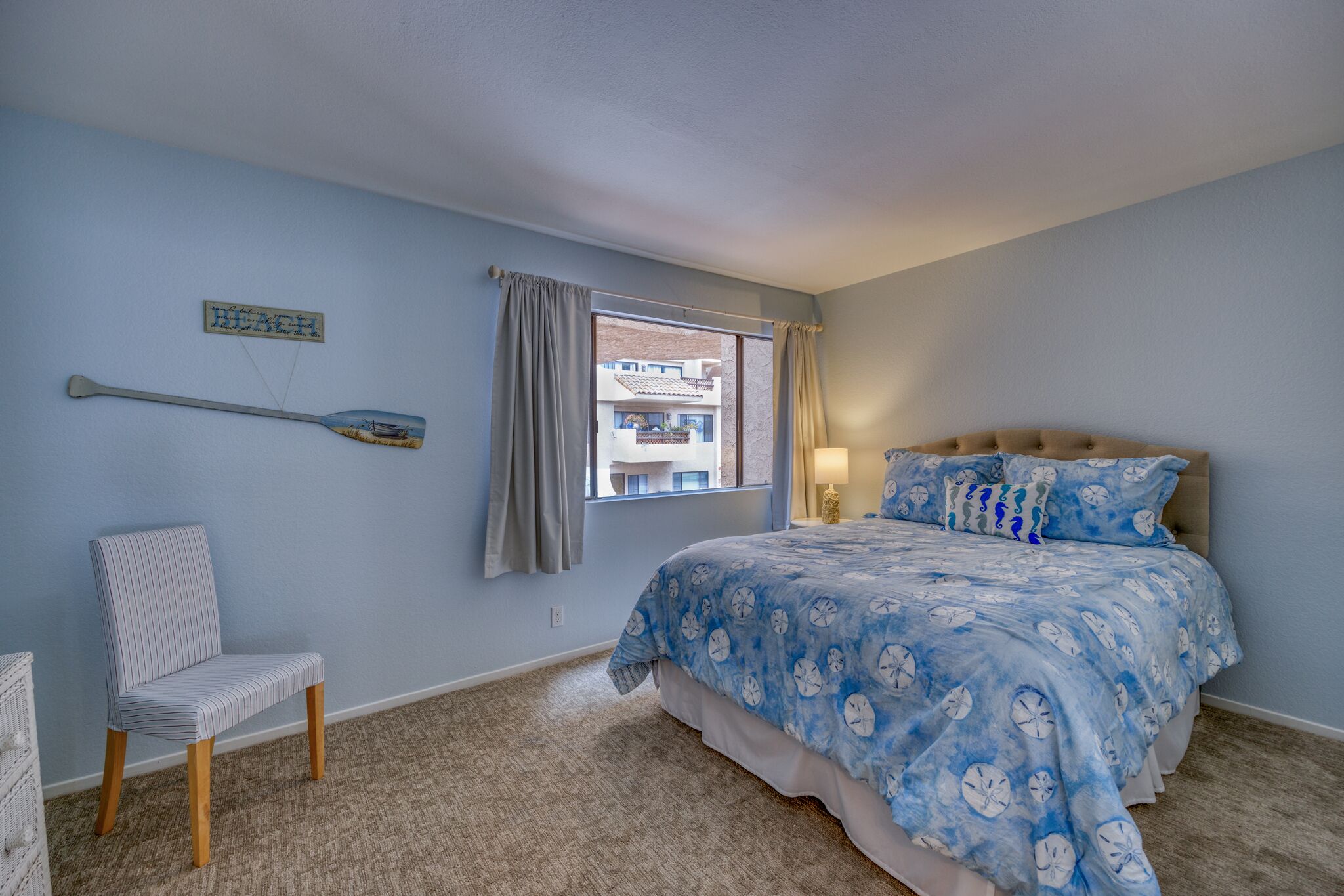 Une chambre à coucher avec un lit, une chaise, une fenêtre avec des rideaux et un tableau accroché au mur.