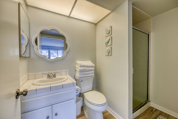 A bathroom with a white sink, vanity, toilet, and a glass shower enclosure.
