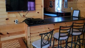 A wooden cabin interior with a bar area, a television mounted on the wall, and a chessboard on a table. - Black Hills Get-Away! (Custer)
