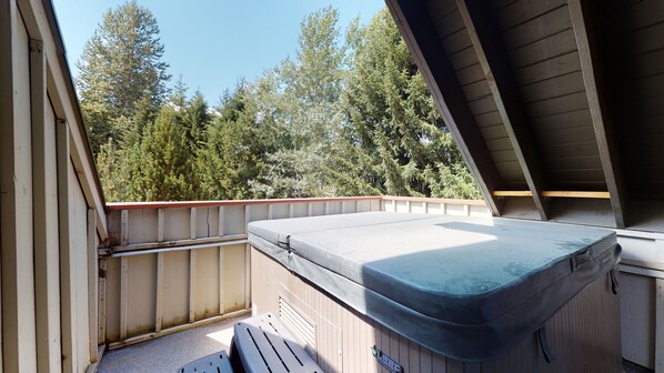 A balcony with a mattress, wooden railings, and a view of trees.
