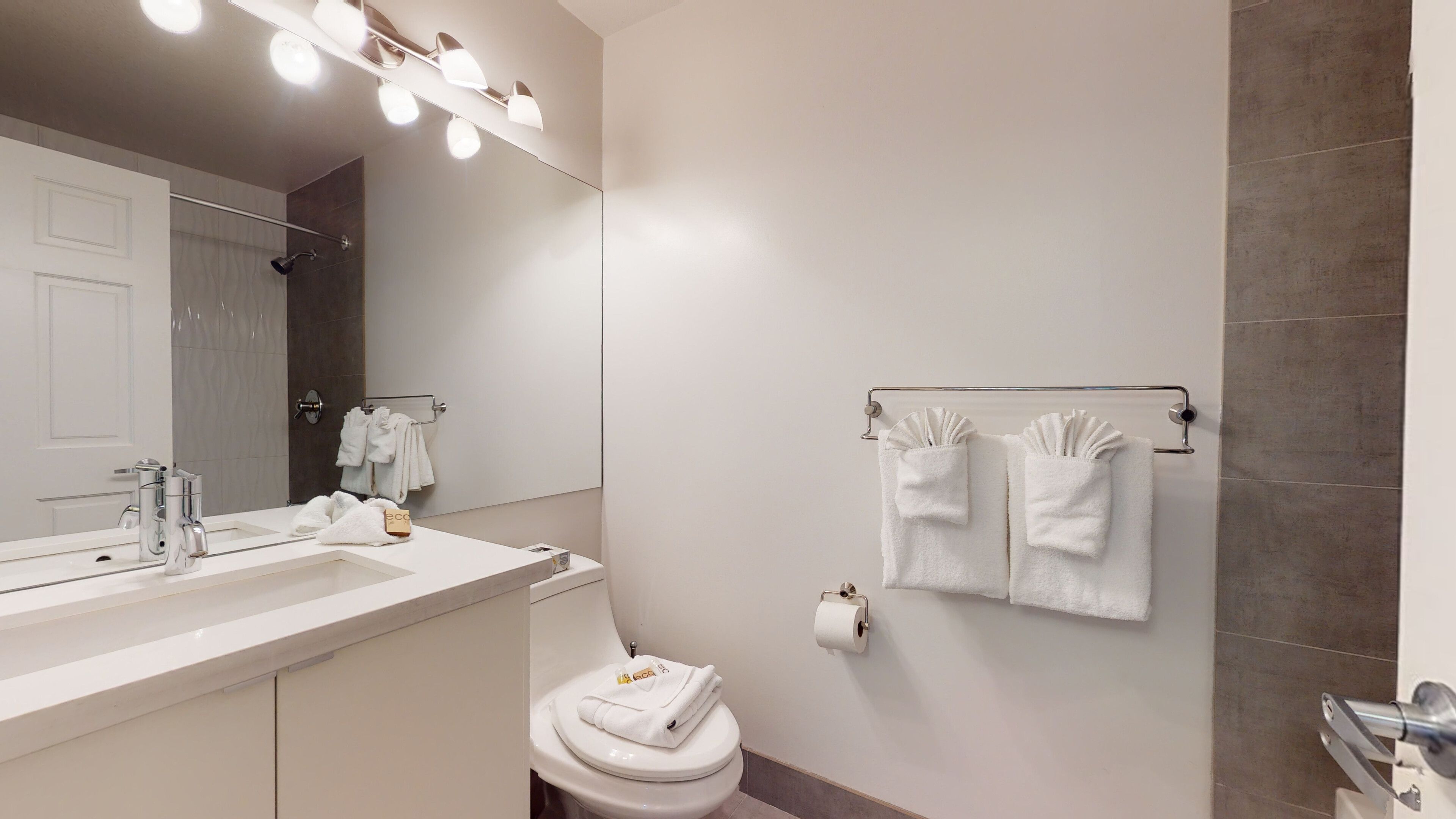 Een moderne badkamer met een grote spiegel, een wastafel met een handdoekhouder, een toilet en een handdoekhouder met opgevouwen handdoeken.