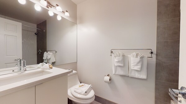 A modern bathroom with a large mirror, a sink with a towel rack, a toilet, and a towel rack with folded towels. - Stoney Creek Sunpath 47 (Whistler)