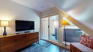 A room with a flat-screen TV on a wooden dresser, a sliding glass door leading to a balcony, and a floor lamp. - Stoney Creek Sunpath 47 (Whistler)