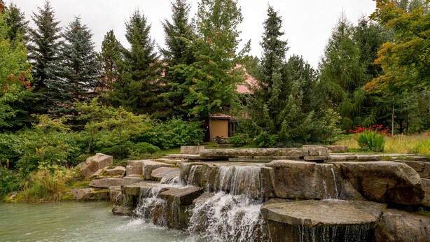 A natural water feature with cascading water over rocks, surrounded by dense greenery and trees. - Renovated, Whistler Village Condo, Private Hot Tub, BBQ & Pool Access. (Whistler)