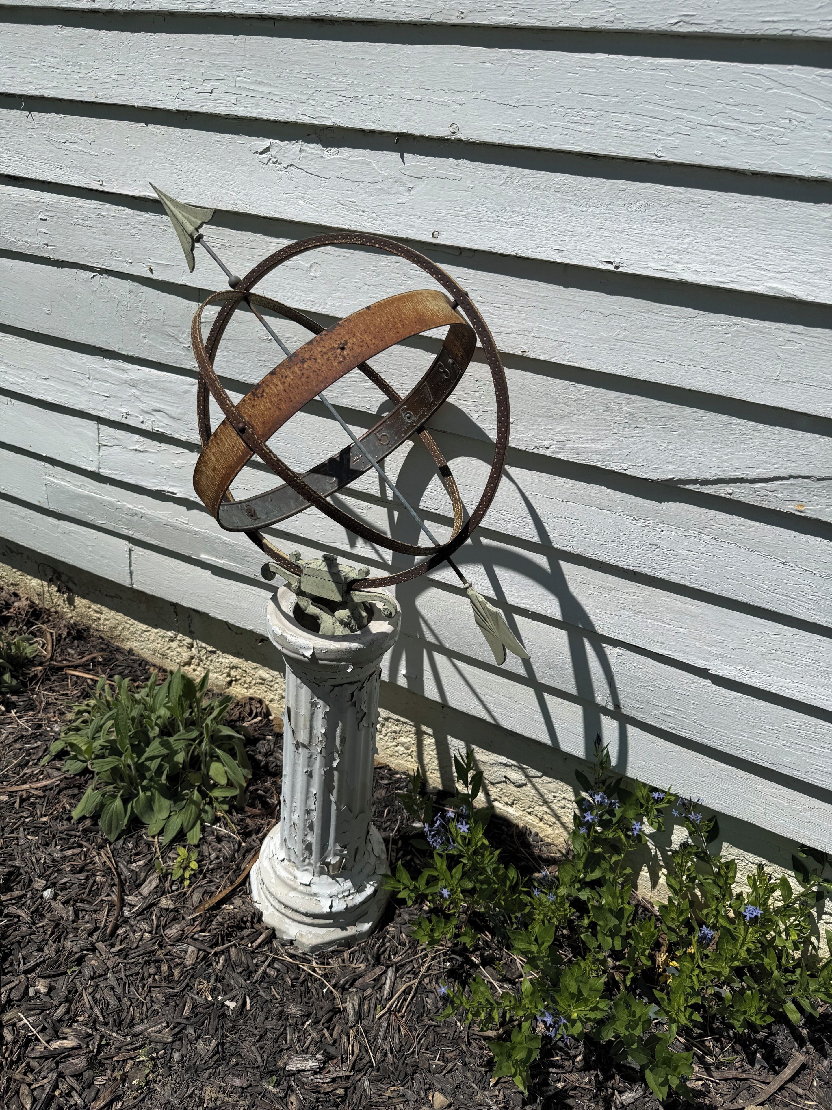 Un objet métallique usé, doté d’un anneau circulaire, qui pourrait être une pièce d’un mécanisme, sur un fond en bois blanc.
