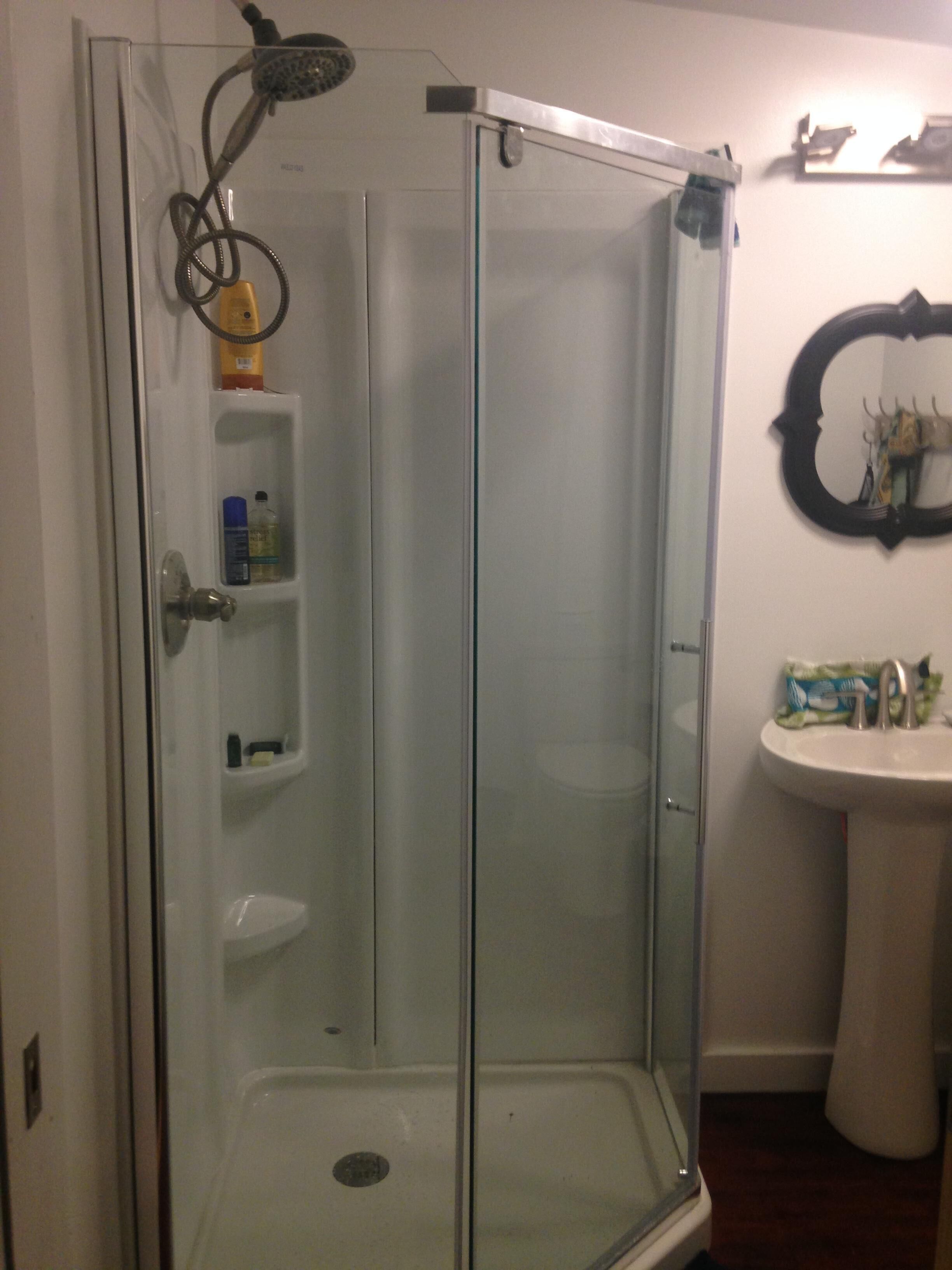 A glass-enclosed shower stall with a built-in shelf holding toiletries.