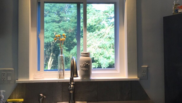 A kitchen with a window, a sink, a faucet, and a vase with flowers.