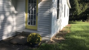Une maison de plain-pied avec une porte jaune, un petit porche et le numéro « 4321 » sur le côté.