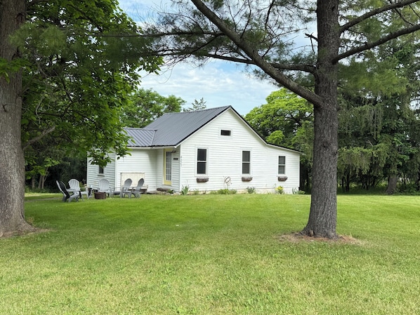 A white single-story house with a gabled roof, surrounded by a well-maintained lawn and large trees.