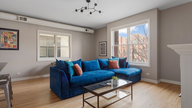 A spacious living room with a blue sectional sofa, a glass coffee table, and a large window offering a view of the city. - The Upscale Getaway Near Downtown (Chicago)