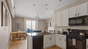 A modern kitchen with white cabinets, a black stove, and a microwave. There is a dining area with a table and chairs. - The Upscale Getaway Near Downtown (Chicago)