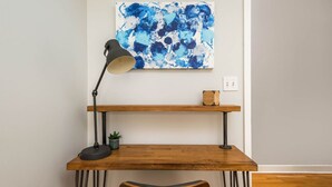 A wooden desk with a black lamp, a small plant, and a blue abstract painting on the wall above. - The Upscale Getaway Near Downtown (Chicago)